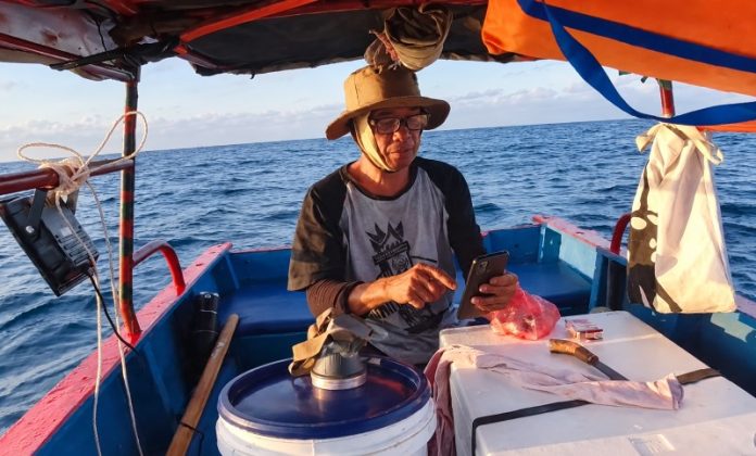 Nelayan Fokus dengan Ponsel di Laut